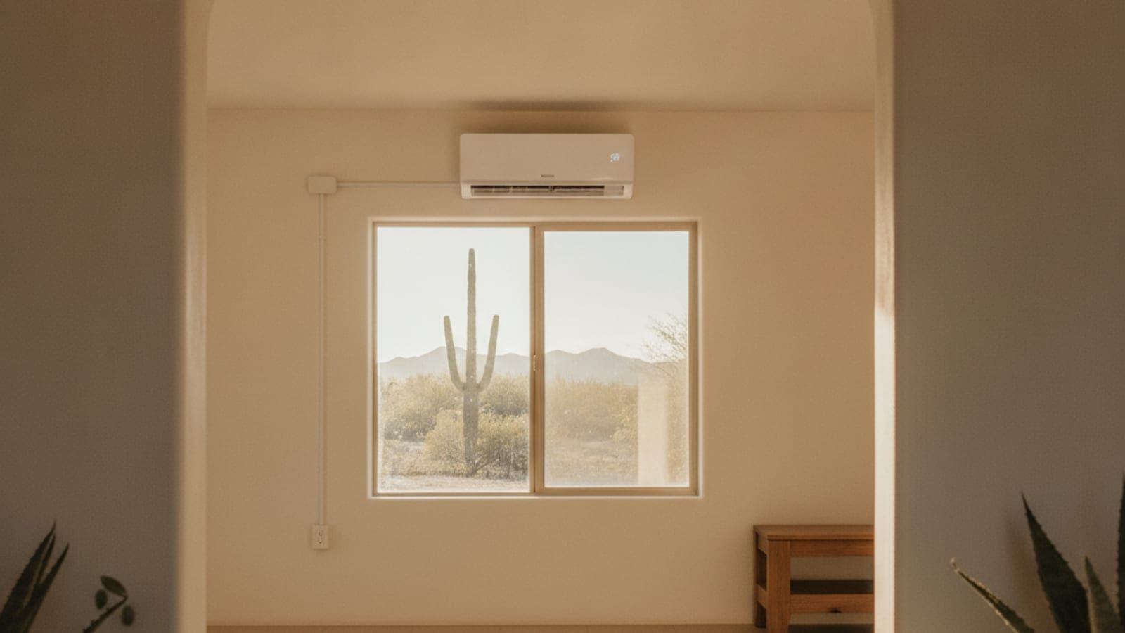 Bright Tucson great room with a wall-mounted mini split above a window and a flat ceiling, saguaro visible outside in warm light