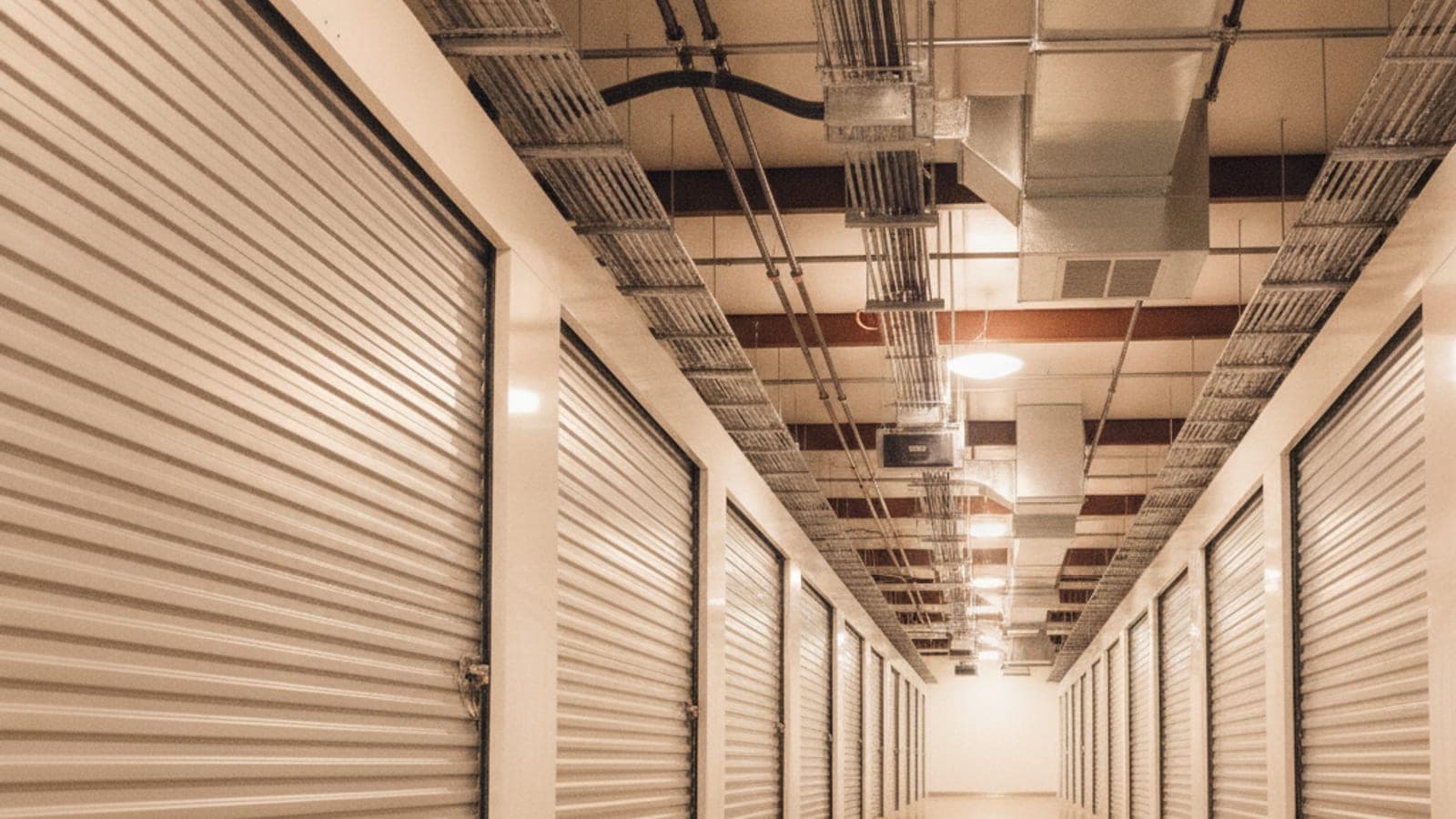 Interior hallway of a climate-controlled storage building with roll-up doors, ceiling ductwork, no people