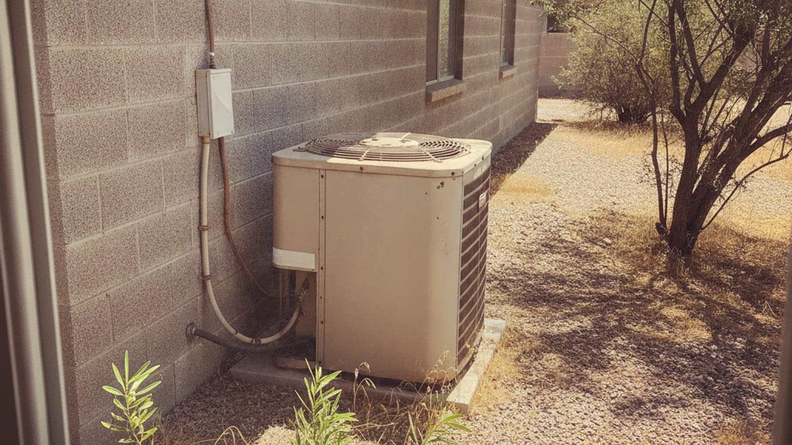 Older AC condenser with faded paint beside a Tucson block home and gravel yard in strong desert sun