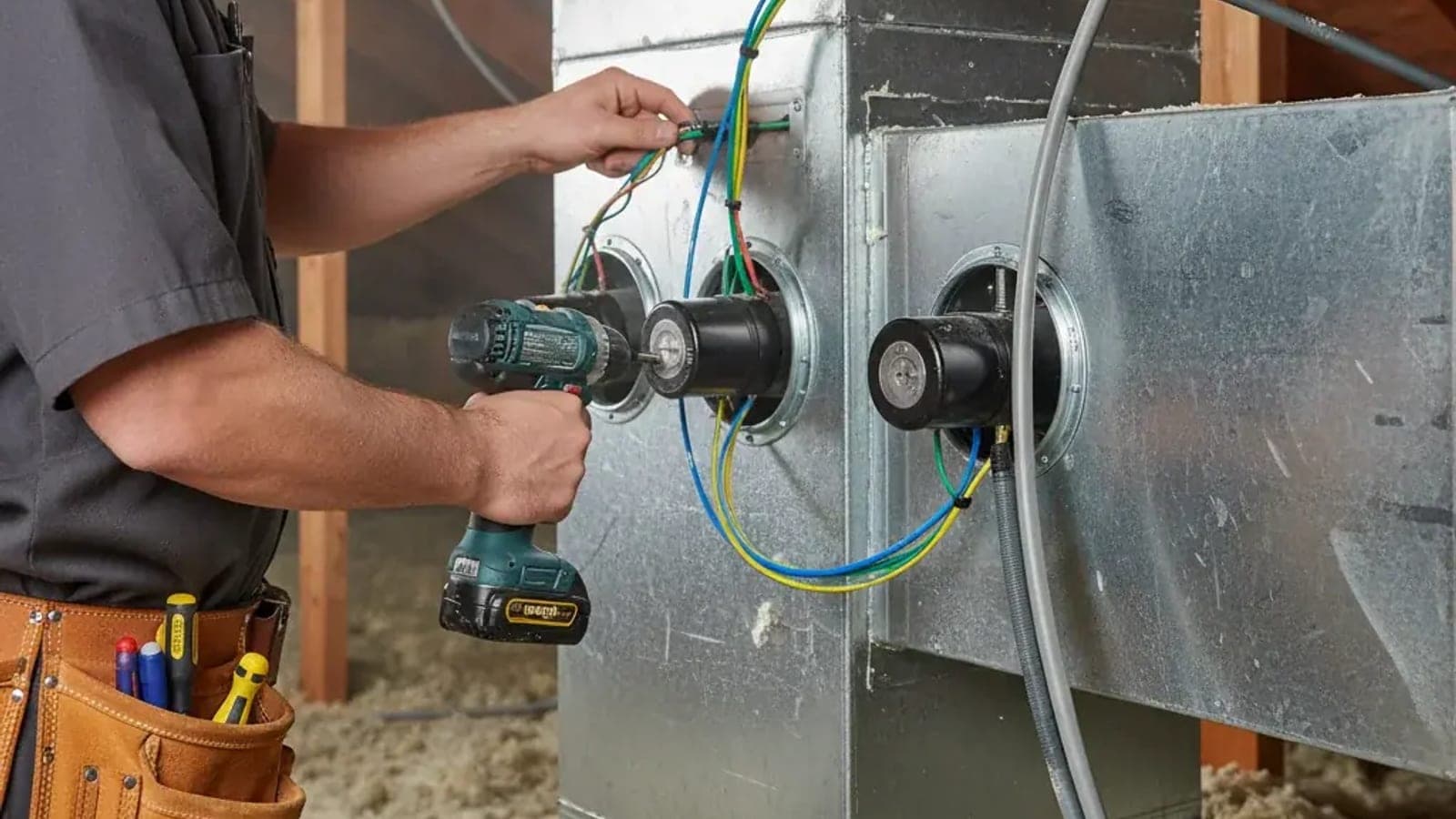 A technician with a drill wiring motorized zone dampers on a sheet-metal duct