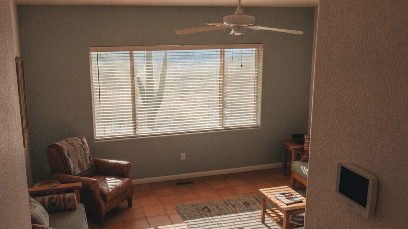 A Tucson living room with blinds half closed, a ceiling fan and a wall thermostat on a summer afternoon