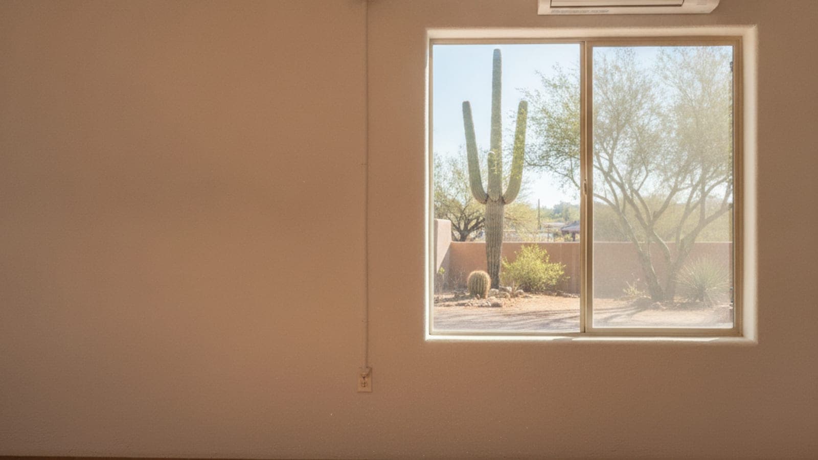 Wall-mounted ductless indoor unit in a bright Tucson casita room with a view of a courtyard with saguaro and palo verde