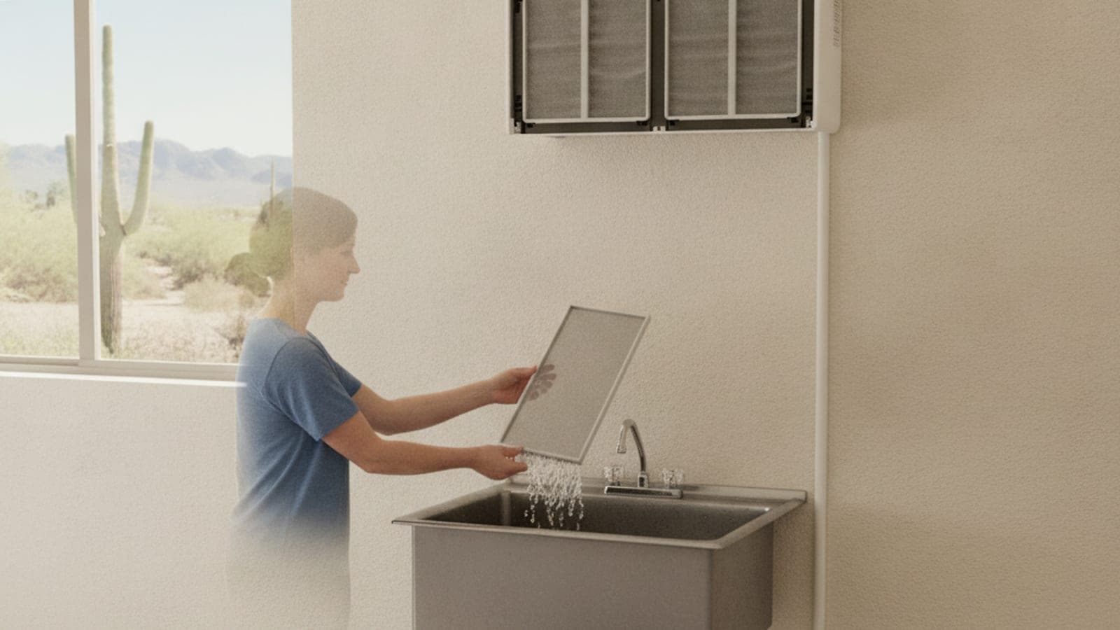 A homeowner rinsing a mini split mesh filter over a utility sink, with a saguaro outside the window